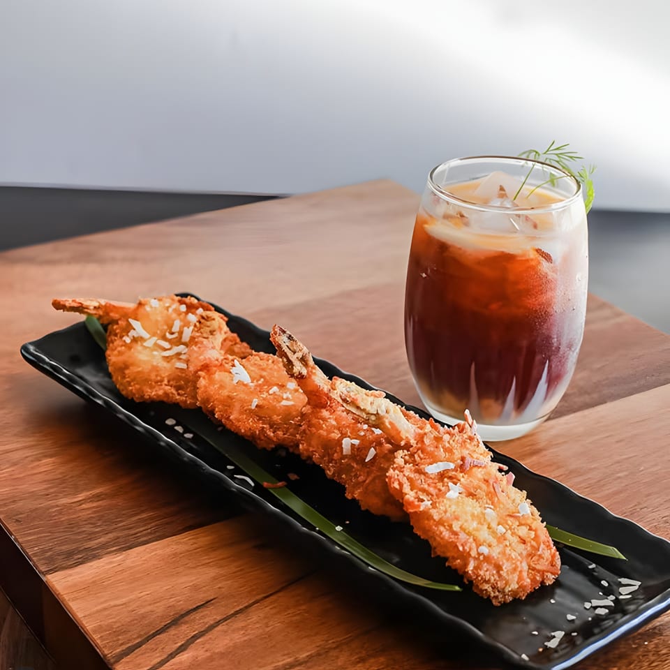 Crispy coconut shrimp on a black plate with green garnish and an iced Thai tea.